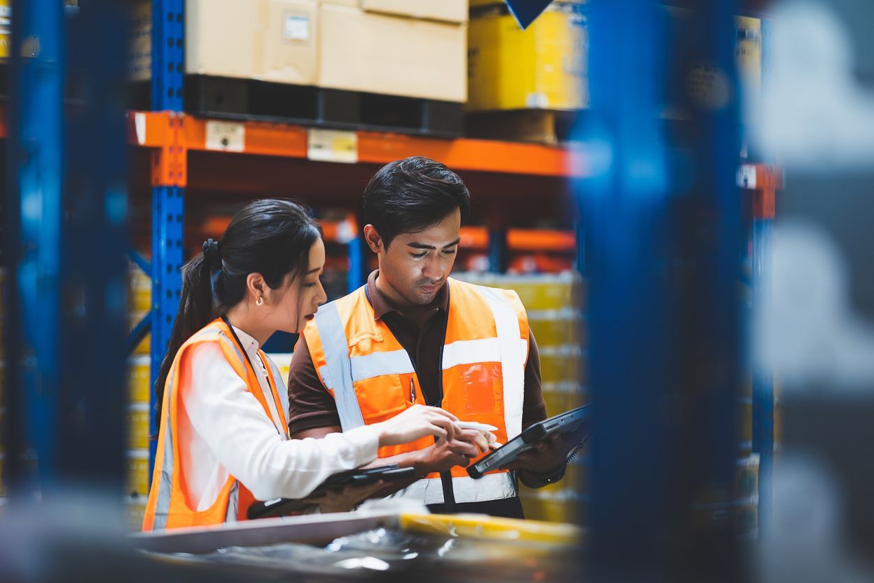 An inventory manager and a warehouse worker checking the quantities of inventories on a tablet in a warehouse