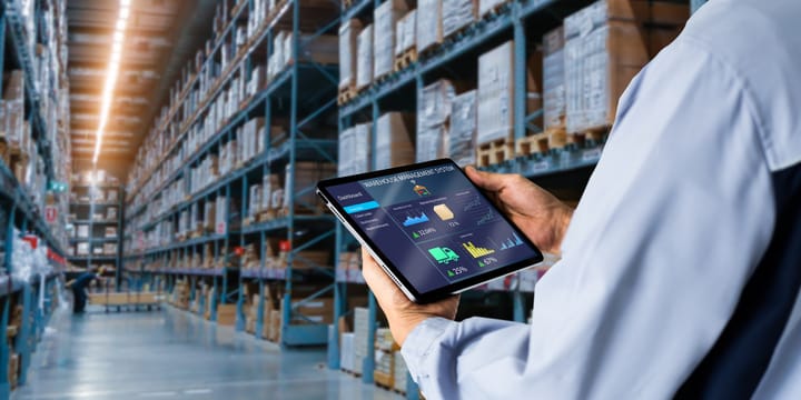 Manager using digital tablet,showing warehouse software management dashboard on blurred warehouse as background.