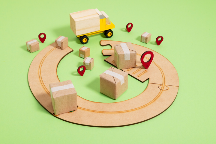 Boxes scattered across the circular wooden puzzle track with a yellow toy van. Light green background.